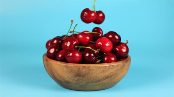 A mans hand take red ripe cherries in wooden bowl on blue background — Stock Video