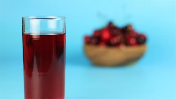 Roter Kirschsaft im Glas und rote Kirschen in Holzschale auf blauem Hintergrund — Stockvideo