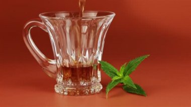Üzerinde kahverengi arka plan cam çay bardağı ve nane dökülür varlık çay yaprakları