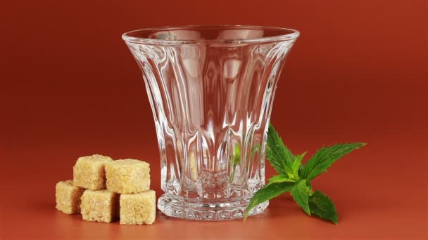 Chá sendo derramado em copo de chá de vidro e açúcar mascavo em cubos com folhas de hortelã no fundo marrom — Vídeo de Stock