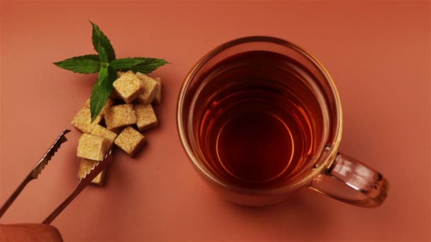 Cubos de azúcar añadidos en el vaso de té sobre fondo marrón — Vídeo de stock