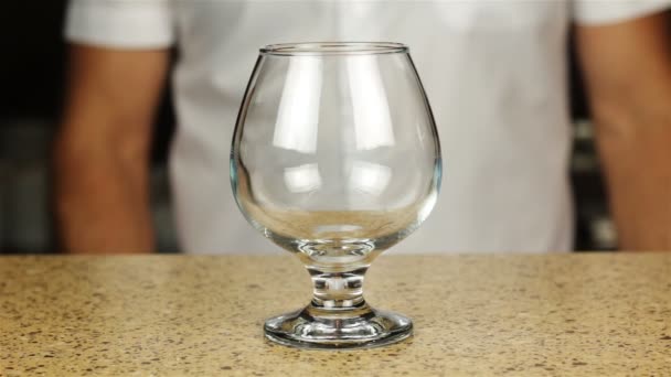 Barman pouring cognac into shot glass with ice on bar table — Stock Video