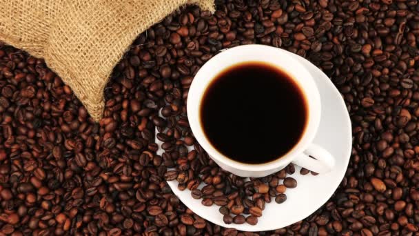 Young man puts a cup of black coffee with roasting coffee beans background — Stock Video