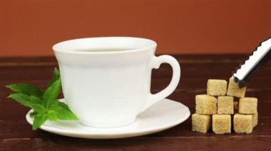 Çay bardağı ve kahverengi şeker küpleri ile nane yaprakları kahverengi ahşap tablo içine eklenen kesme şeker