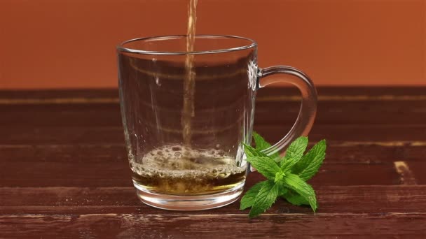 Thé versé dans une tasse à thé en verre et feuilles de menthe sur une table en bois brun 