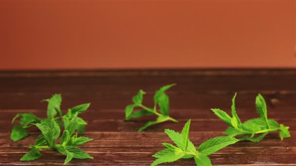 Un homme met un verre de thé glacé à la menthe et au citron, des glaçons sur la table avec des feuilles de menthe fraîche sur une table en bois marron — Video