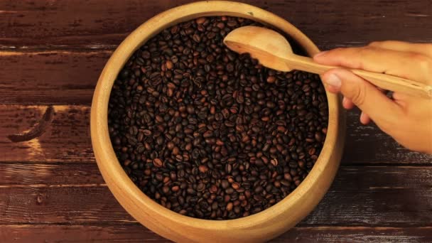 Kaffebönor i en träplatta rör om med en sked på brun träbord — Stockvideo