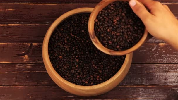 Coffee beans in wooden plate pouring in a large wooden bowl of coffee beans on brown wooden table — Stock Video