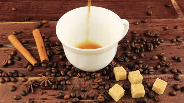 Verter una taza de café en la mesa ubicados granos de café, terrones de azúcar morena y palitos de canela sobre la mesa de madera marrón — Vídeos de Stock