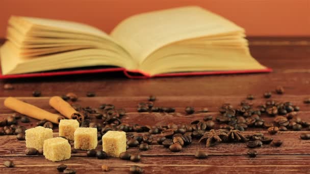 Um homem coloca uma xícara de café sobre a mesa, sobre ele localizado grãos de café, livro aberto, cubos de açúcar mascavo e paus de canela sobre mesa de madeira marrom — Vídeo de Stock