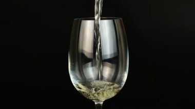 Beyaz şarap siyah arka planda cama dökülüyor.