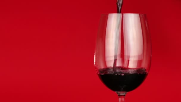 Vino tinto vertido en vidrio sobre fondo rojo — Vídeo de stock