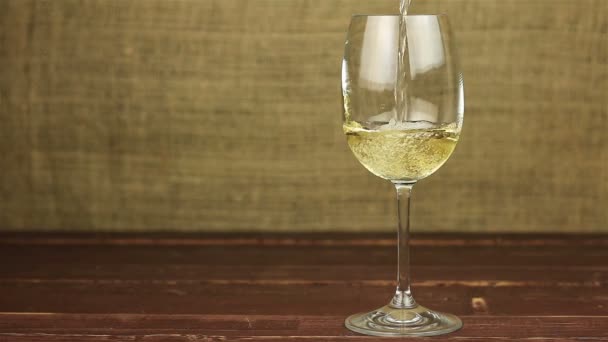 Vino blanco vertiendo en un vaso sobre una mesa de madera — Vídeos de Stock