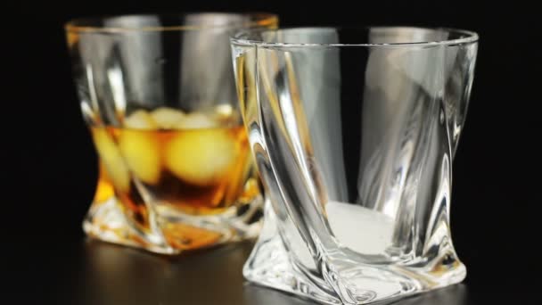 Whisky wird in ein Glas mit Eis vor schwarzem Hintergrund gegossen — Stockvideo