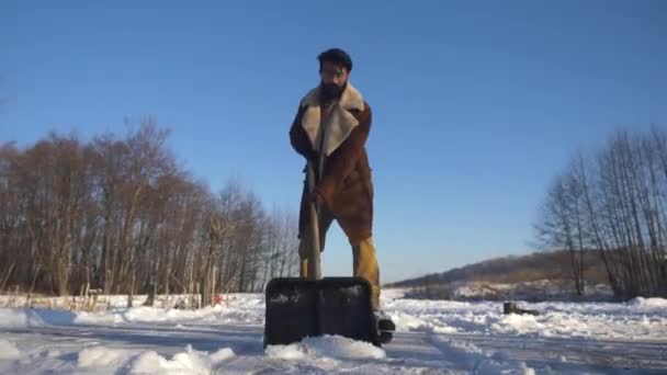 Seorang pemuda India di skates Membersihkan salju dengan sekop di danau beku. — Stok Video