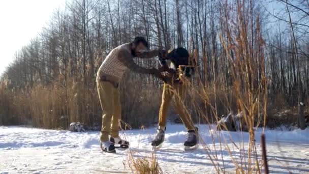 Dos chicos indios y europeos aprenden a patinar en un lago congelado y a hacer travesuras. — Vídeo de stock