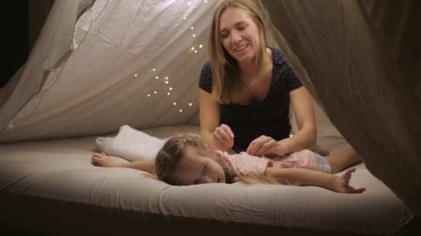 Boldog anya ad a lányának egy hátmasszázst egy sátorban otthon, mosolyognak és nevetnek. — Stock videók
