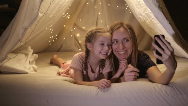 Glückliche Mutter und Tochter rufen ihren Vater aus einem provisorischen Zelt zu Hause an, sie lächeln und reden, in einer Zeit der sozialen Isolation. — Stockvideo