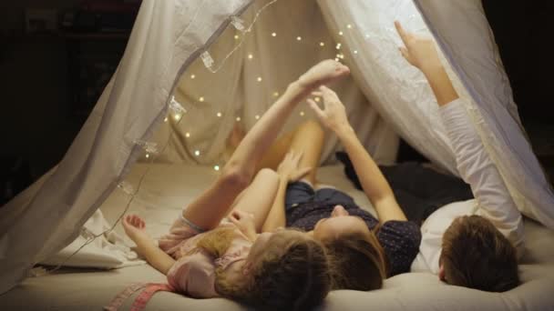 Bonne maman aime les vacances en famille avec ses enfants fils et fille, devinez les constellations d'ampoules dans une tente dans le salon, s'éloigner de la société — Video