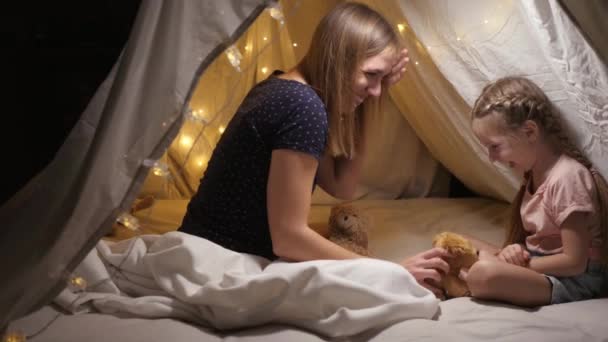 Boldog anya élvezi a családi időt a lányával, ölelkezik egy sátorban a nappaliban, játszik egy plüss kutyával — Stock videók