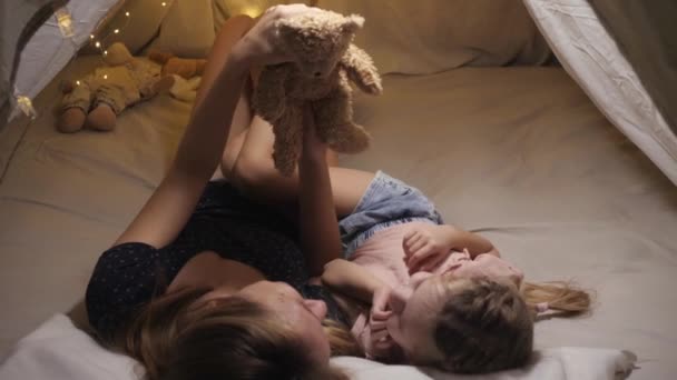 Lycklig vit kvinna njuter av familjetid med sin dotter, de skrattar och pratar med en nalle i ett handgjort tält — Stockvideo