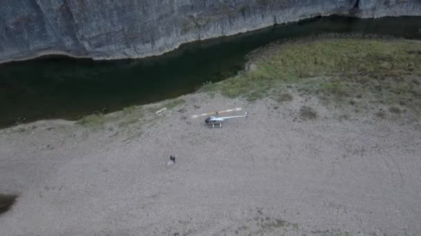 Helikoptéra s točícími se čepelemi v přírodě u řeky a skálou se začíná vznášet. Nedaleko je mladý pár zamilovaný. — Stock video
