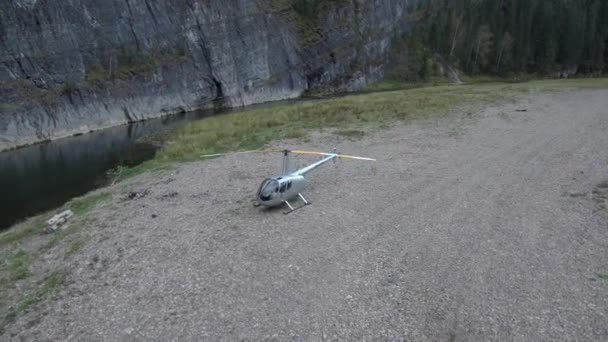 Vrtulník stojí na břehu řeky pod skálou a začíná otáčet lopatkami.. — Stock video