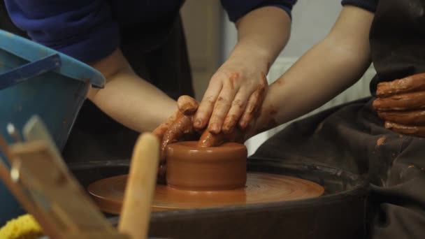 Close-up van volwassen en kinderen vuile handen gieten klei in keramische pot op gooien wiel werken binnen. Creatieve activiteit en traditioneel ambachtelijk concept. — Stockvideo