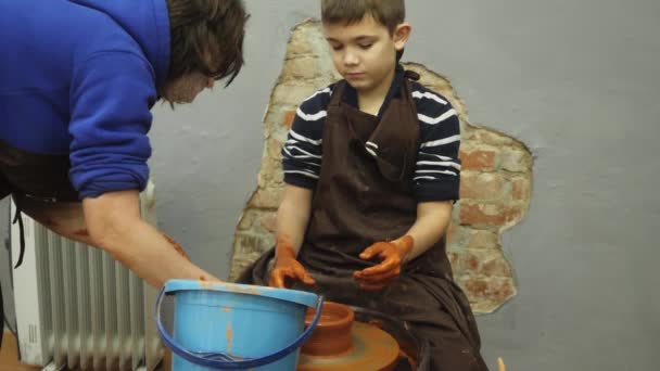 Primer plano de adultos y niños manos sucias moldeando arcilla en maceta de cerámica en el lanzamiento de la rueda de trabajo en interiores. Conceptos de: experiencia, arte, tradición, familia. — Vídeo de stock