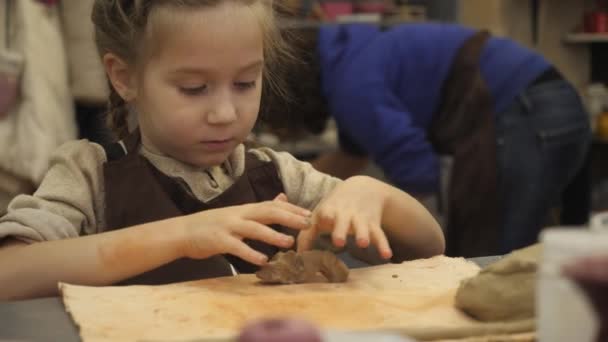 En ung keramiker barn flicka skulpterar från en bit vit lera en tom för den framtida mugg. Hon försöker mycket hårt och visar sina känslor i ansiktet. — Stockvideo