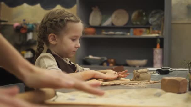 En ung keramiker barn flicka skulpterar från en bit vit lera en tom för den framtida mugg. Hon försöker mycket hårt och visar sina känslor i ansiktet. — Stockvideo