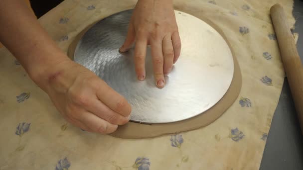 Närbild av händerna på en Potter som skär bort överflödig vit lera, gör en tom för den framtida plattan. — Stockvideo