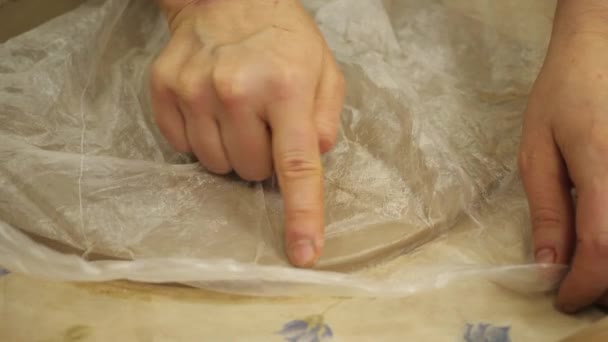 Närbild av mästarens hand, som använder en plastpåse för att rikta de skarpa kanterna på lerplattan. — Stockvideo