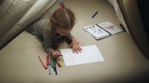Geçici bir kulübede küçük bir kız beyaz bir kağıt parçasına resim çiziyor. Coronavirus salgını sırasında. — Stok video