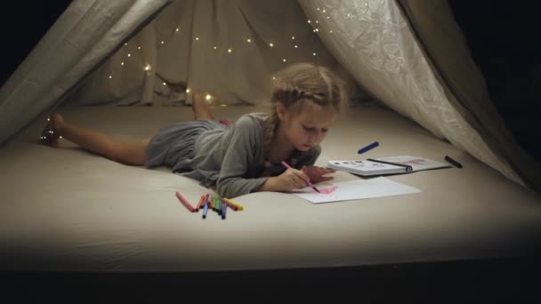 En liten flicka i en provisorisk hydda ritar på ett vitt papper. Under Coronavirusets pandemi. — Stockvideo