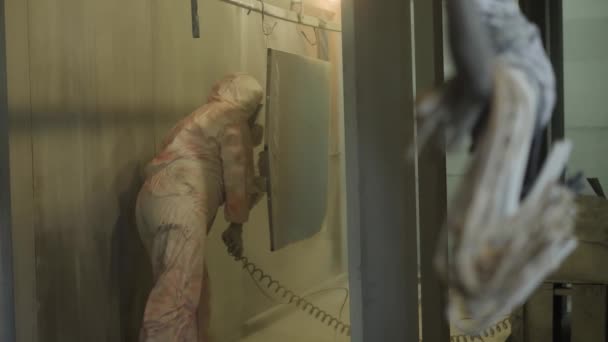 Worker in protective suit sprays powder paint from gun on metal products — Stock Video