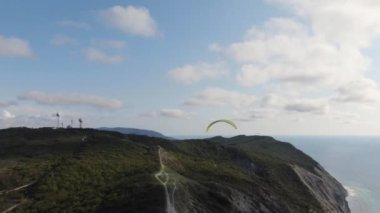 Bir paraglider denizin kenarındaki bir kayanın üzerinden uçuyor..
