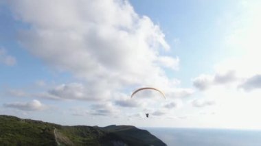 Bir paraglider denizin kenarındaki bir kayanın üzerinden uçuyor..