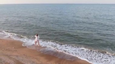 Islak tişörtlü mutlu bir kız kumsalda ve deniz kıyısında koşar.