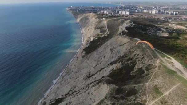 Bir paraglider denizin kenarındaki bir kayanın üzerinden uçuyor.. — Stok video
