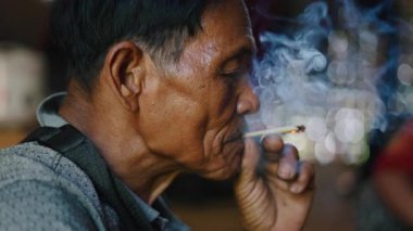 Close-up asian man lahu calm and relaxed senior lighting a handmade cigarette in traditional way - 4K Horizontal