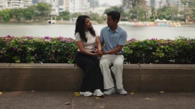 Young loving couple sitting on a bench by a lake, holding hands and having a heartfelt conversation