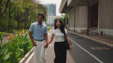 Young romantic couple walking hand in hand along a city street on a sunny day