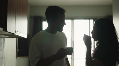 Romantic young asian couple silhouette chatting and drinking coffee together in the kitchen at home