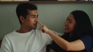 Happy young asian couple laughing and cuddling together on a sofa in their living room at home