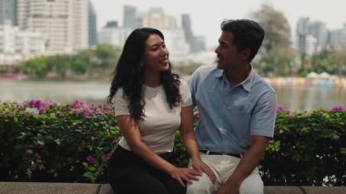 Loving young boyfriend and girlfriend sit together talking and cuddling on a date in a park