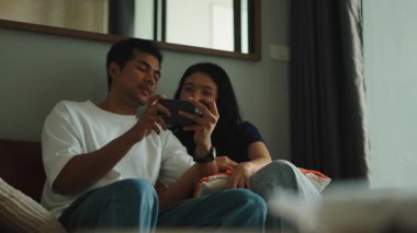 Happy young couple sitting on a sofa and playing a mobile video game together in their apartment