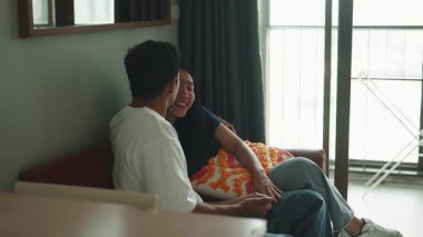 Romantic asian couple sitting on a couch, laughing and talking together in their living room