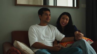 Young asian man and woman watching a movie, talking, and laughing together on the sofa at home