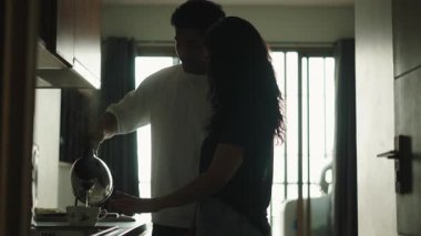 Silhouette of a happy young couple preparing a hot drink in the kitchen during a quiet morning